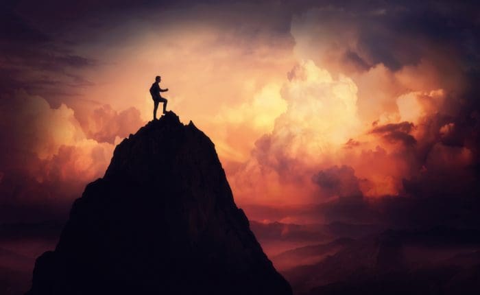 Person who overcame addiction barriers standing triumphantly on top of tall mountain
